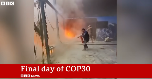 A man wields a fire extinguisher as flames burn inside the COP30 pavillion